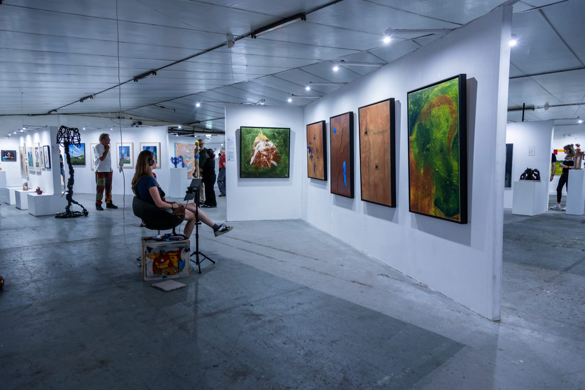 An exhibition room with visitors and framed paintings by Ward Schepman.